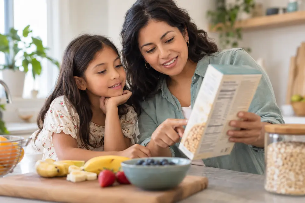 Una madre y su hija leen juntas un envase de alimento en la cocina.